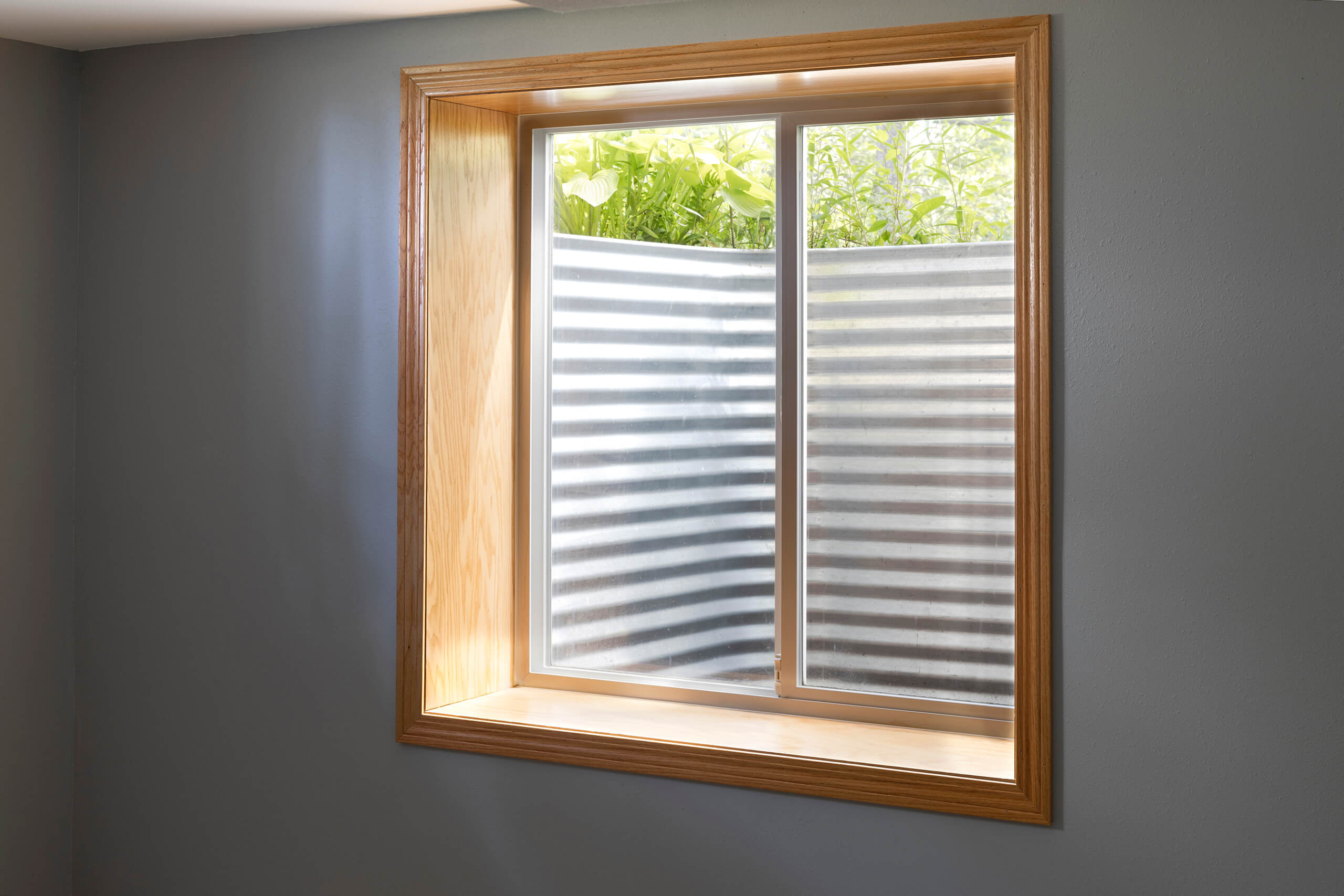 Basement egress window with metal window well and wood trim.